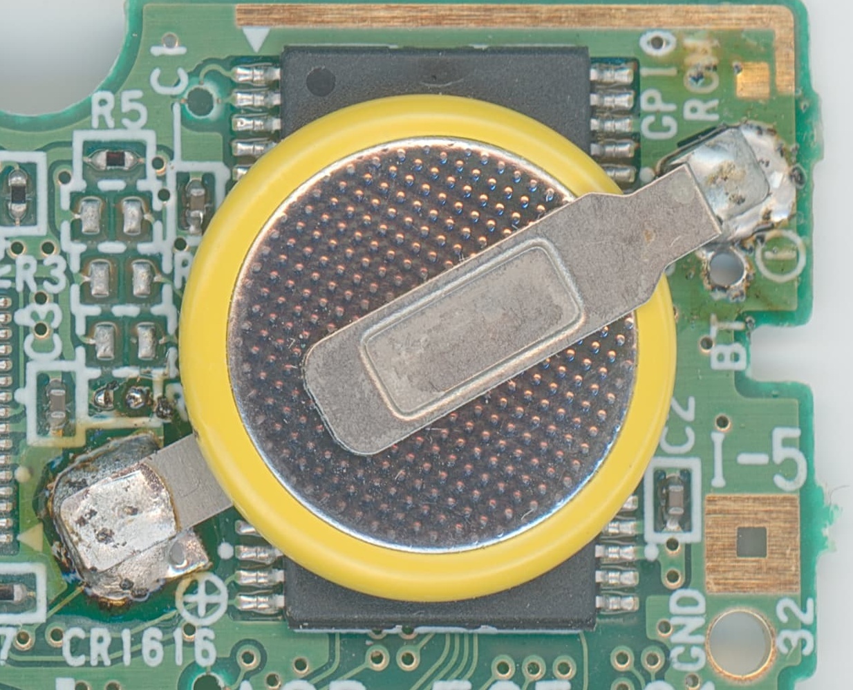 Close-up of the round yellow-rimmed coin battery and metal solder tabs on an English Pokémon Ruby board
