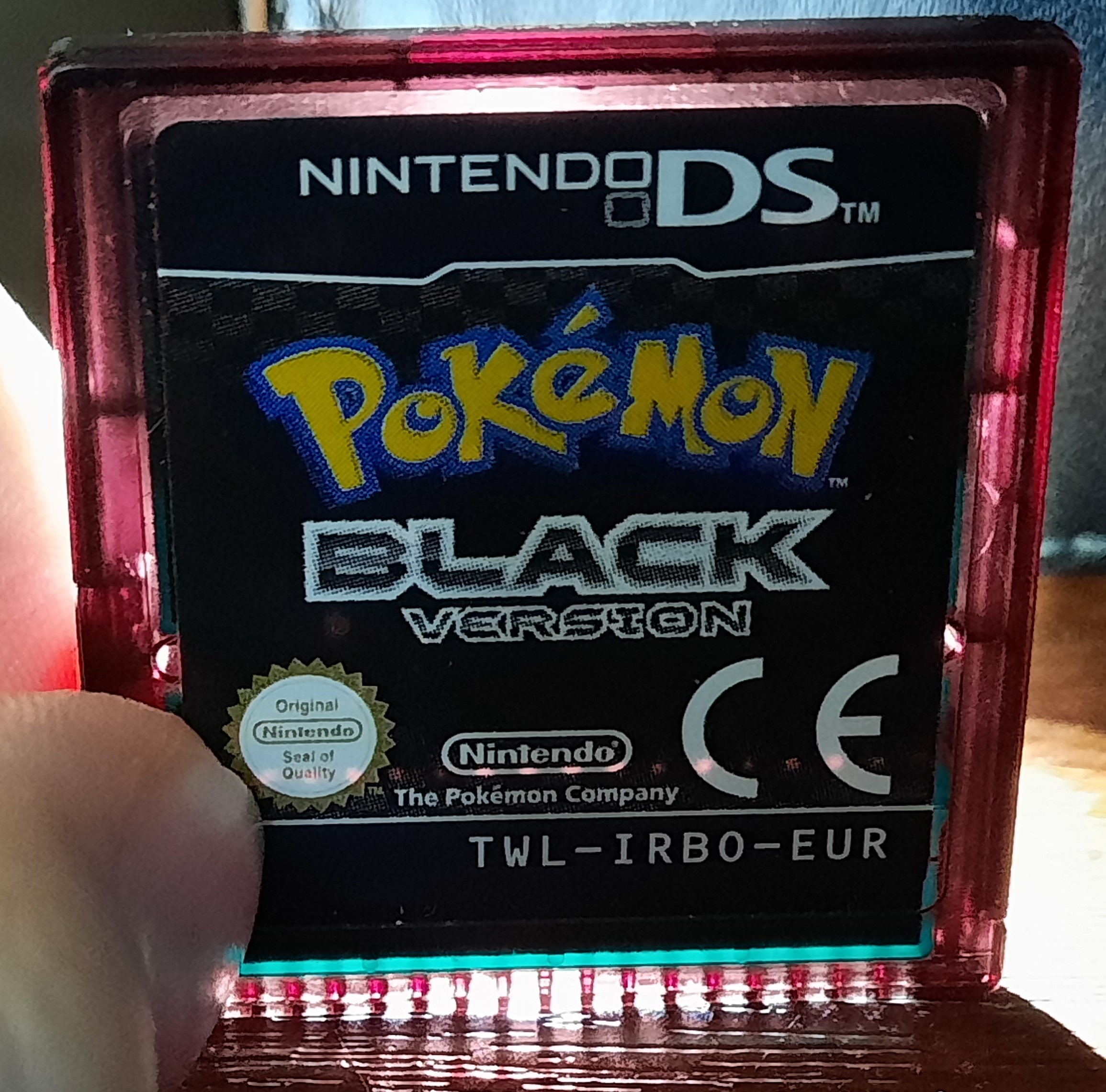English European Pokémon Black cartridge illuminated from behind, showing its red translucent infrared shell and TWL-IRBO-EUR code